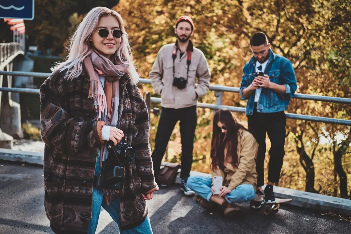 Ein attraktives blondes Mädchen mit einer Fotokamera genießt einen Herbstspaziergang mit ihren Freunden.